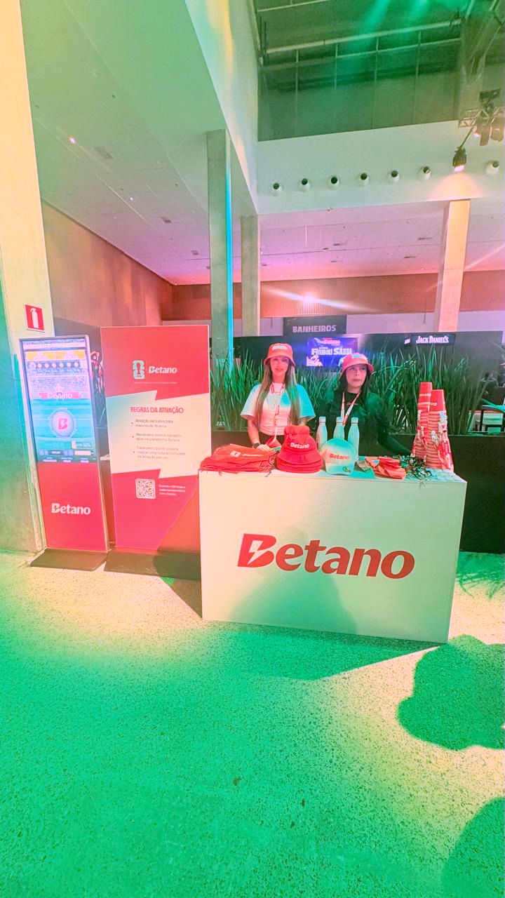 Totem digital ao lado de estande de ativação de marca com equipe e brindes