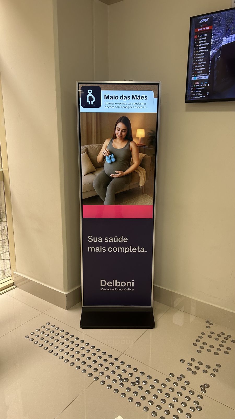 Totem digital em recepção de clínica exibindo campanha de saúde